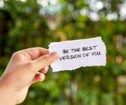 hand holding a paper slip that reads "Be the Best Version of You", with trees out of focus in the background