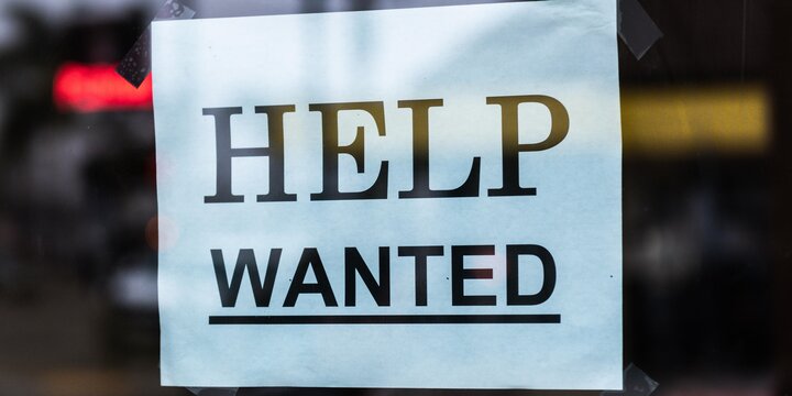 Sign reading "Help Wanted" behind glass