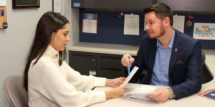 A career coach talks to a student while pointing to their resume at a desk