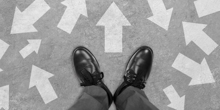 Feet in dress shoes with arrows on the ground pointing in multiple directions