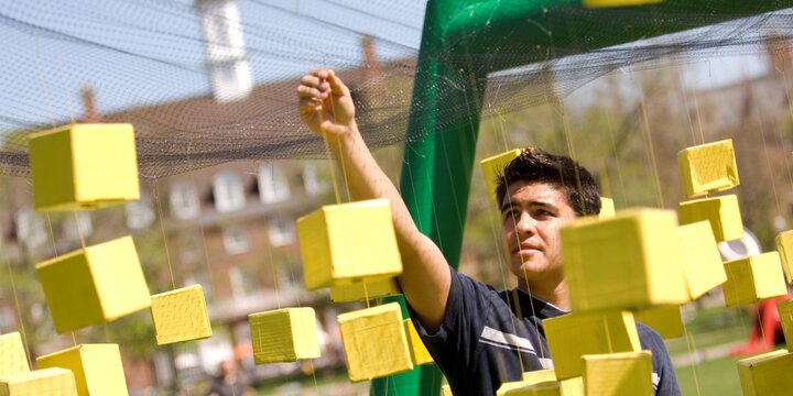 a student hangs large yellow blocks on an obstacle course on the Illinois quad, with the Illini Union building visible in the distance