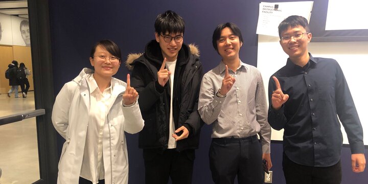 four international students holding up index fingers 
