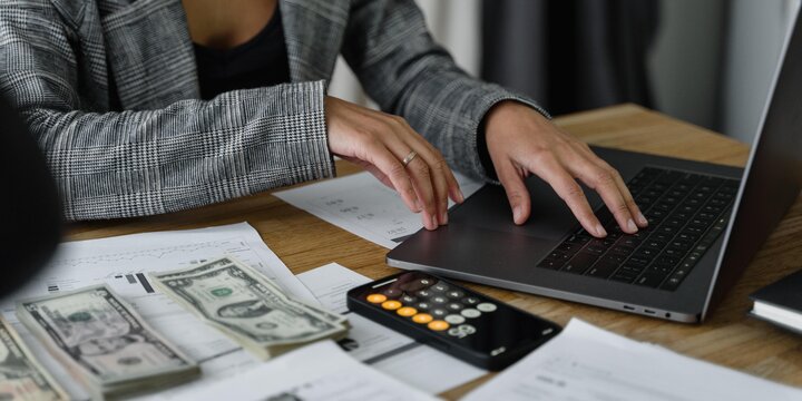 woman sitting at table with laptop, calculator, paperwork and money neatly stacked in piles