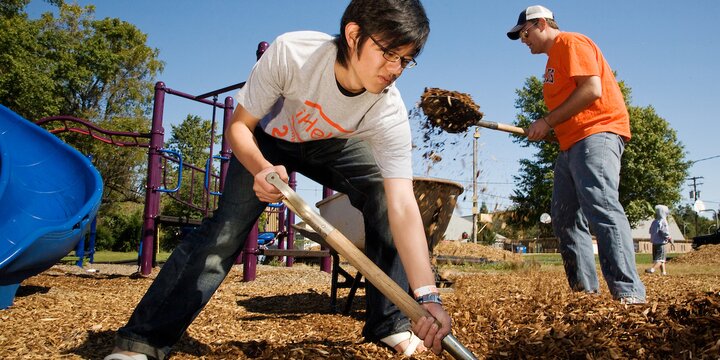 Two Student volunteers wearing iHelp shirts shovel mulch in a playground