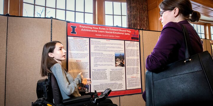 a student in a wheelchair presents a poster at the undergraduate research symposium