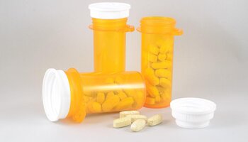 Three orange prescription bottles, one with the lid off, and a few loose pills
